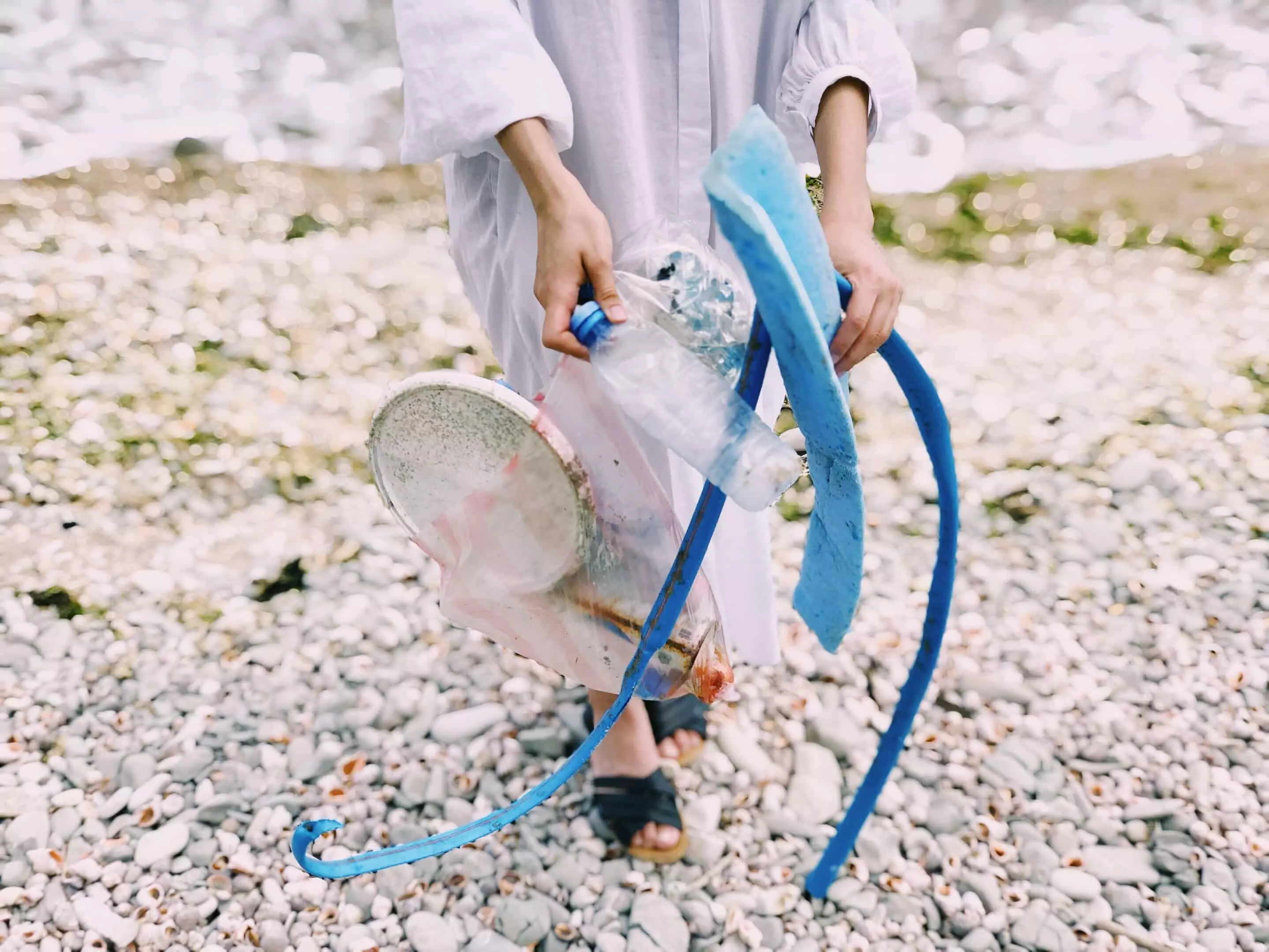 Person am Kiesstrand mit diversen angespülten Plastikfundstücken in den Händen