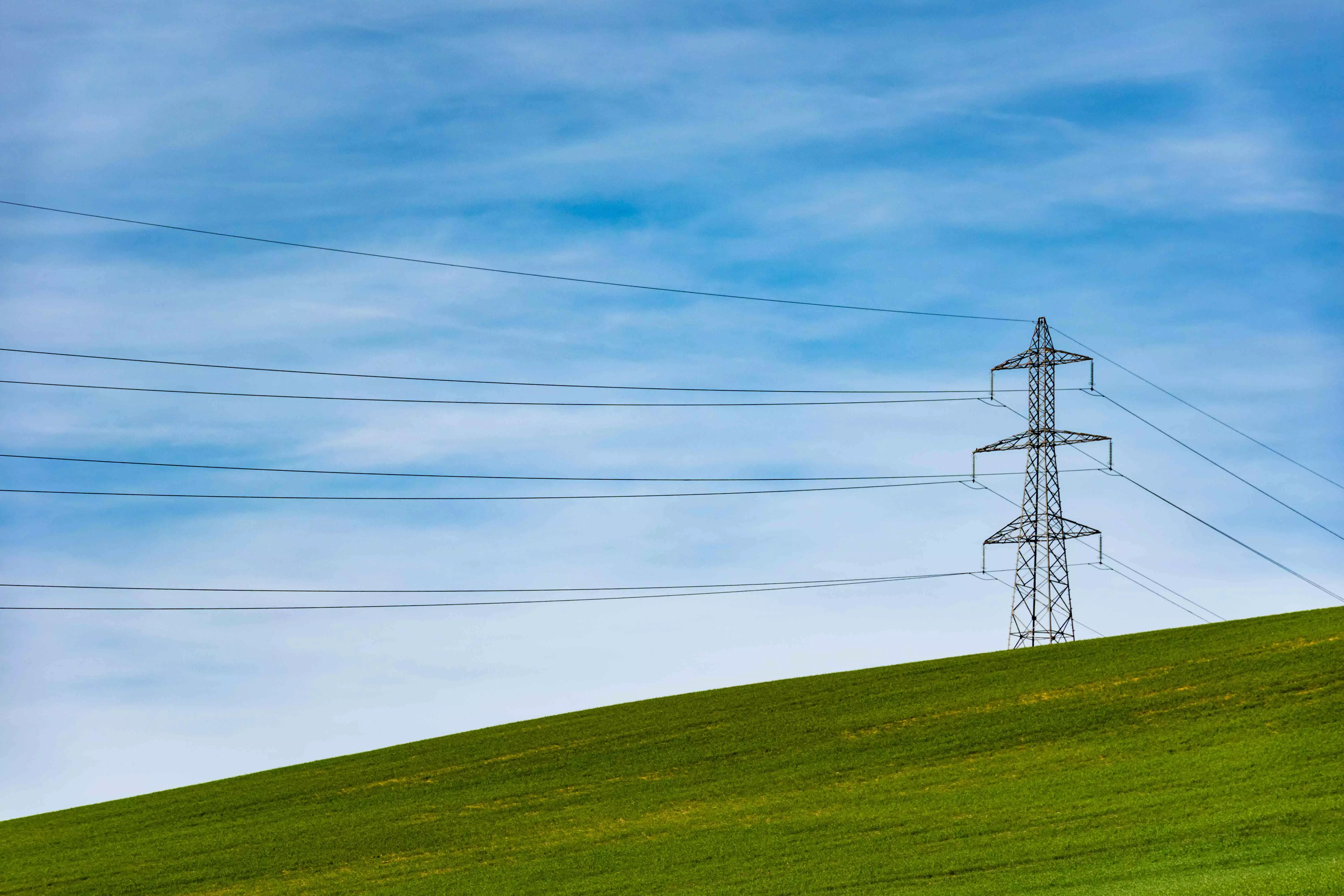 Strommast auf hügeliger Wiesenlandschaft