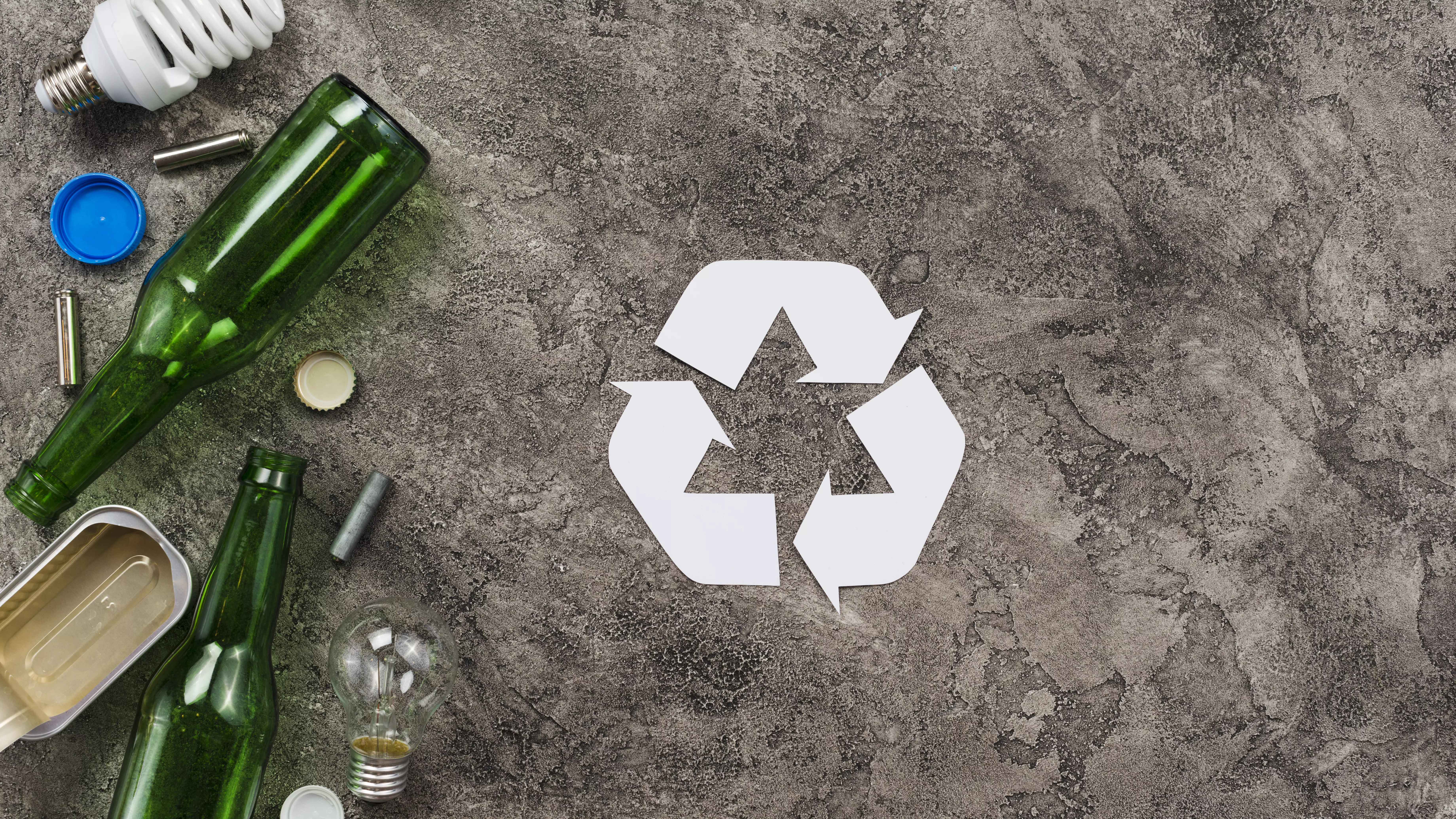 Verschiedener Müll auf Steinuntergrund mit weißem Recycling-Zeichen
