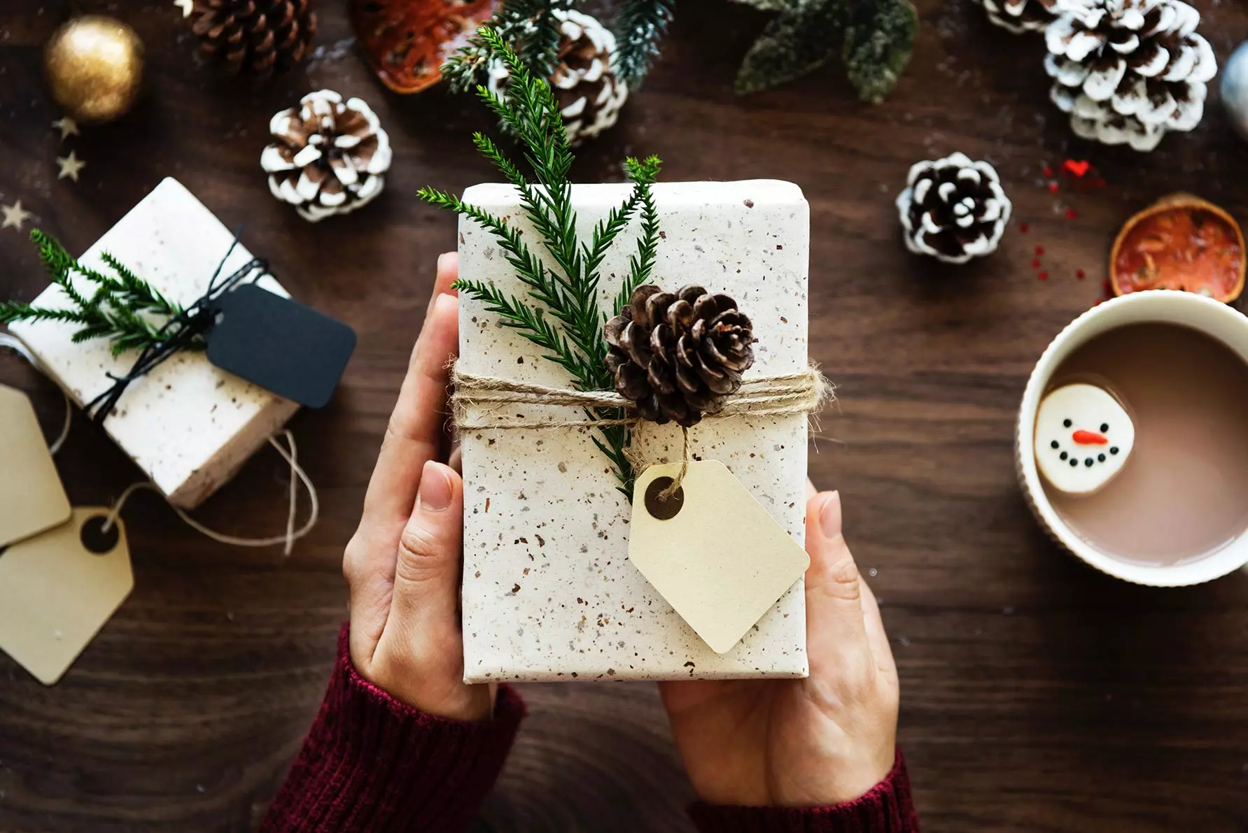 zwei Hände halten ein verpacktes Geschenk in weihnachtlicher Deko