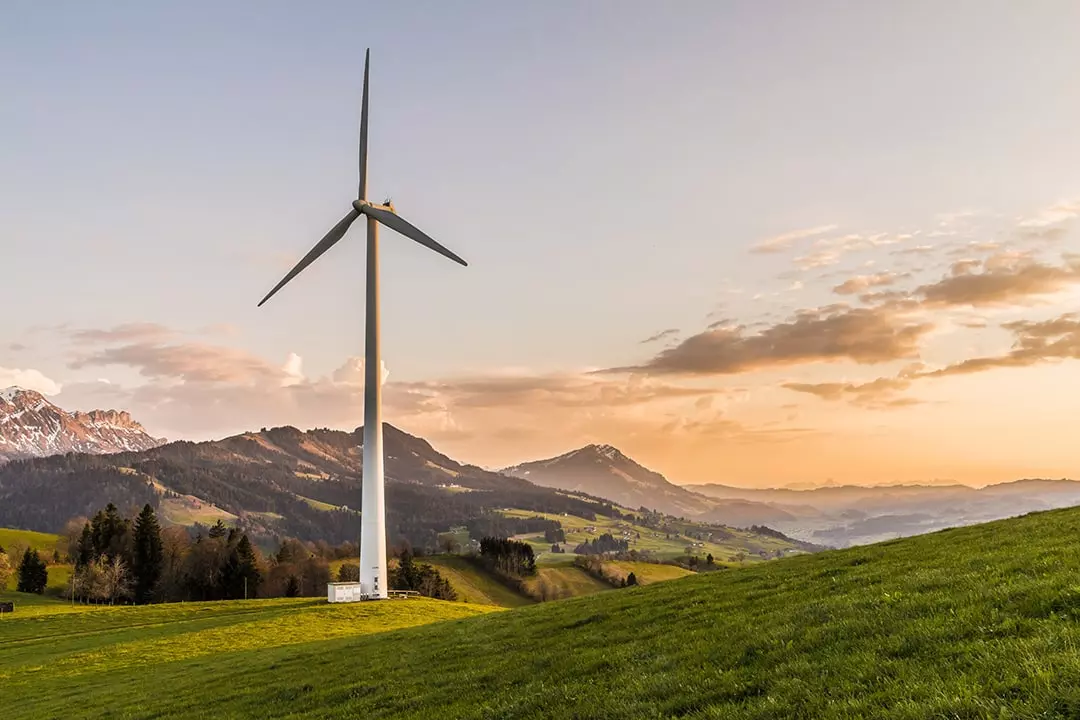 Windrad auf hügeliger Wiese in morgendlicher Berglandschaft